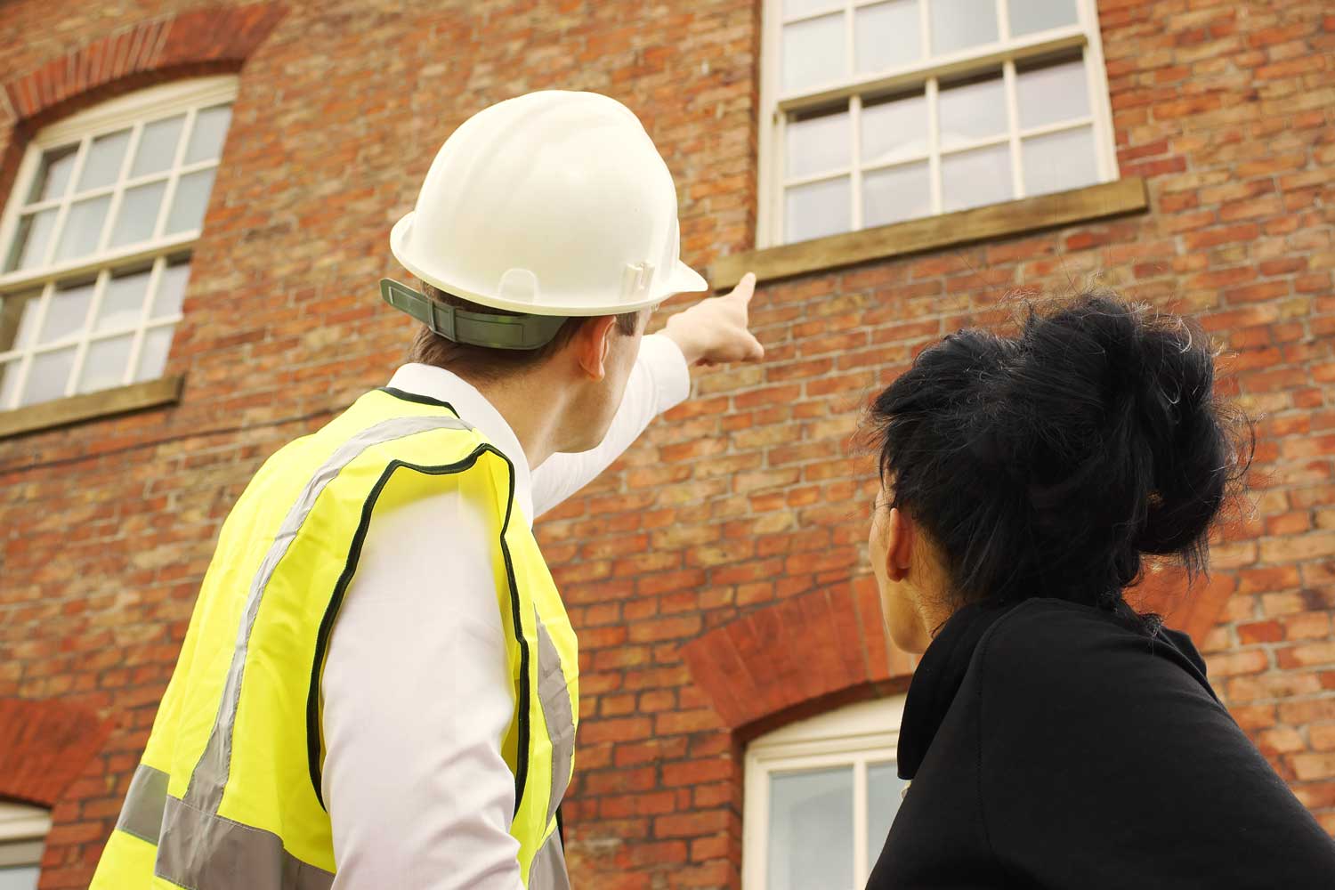 Surveyor and customer looking at red brick house with sash windows